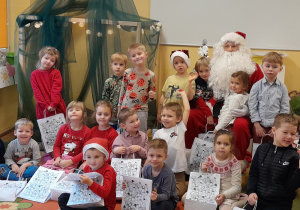 Dzieci zgromadzone przy Świtym Mikołaju. Niekóre dzieci trzymają w dłoniach torebki z preznetami od Mikołaja.